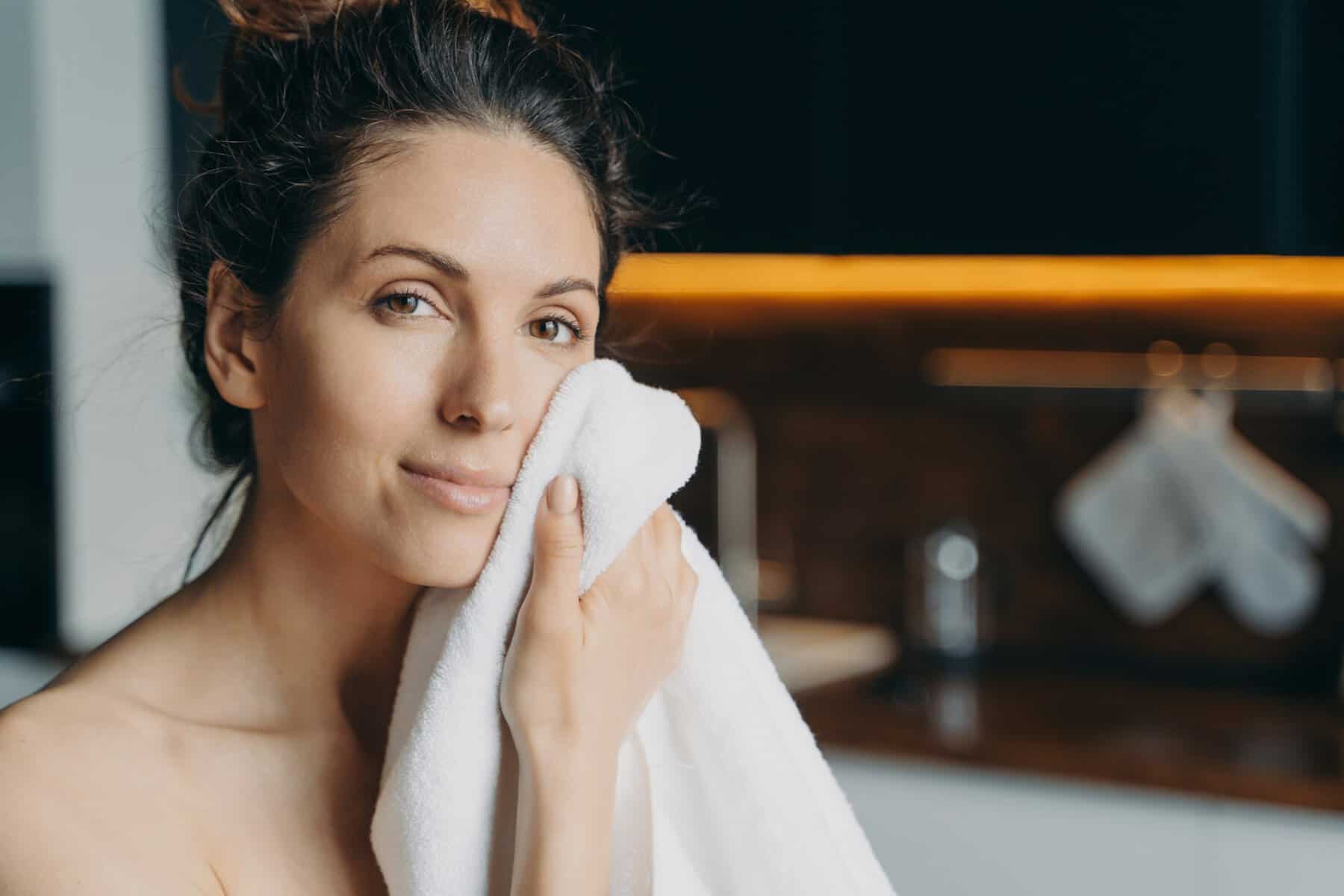 Pretty girl wipe face with towel after shower, enjoy healthy smooth skin at home. Hygiene, skincare